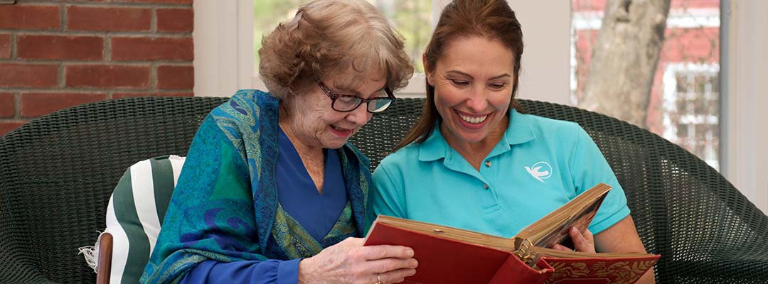 Female home care worker looks through old photo album with senior woman at home.